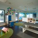 Interiørfoto av en avdeling i barnehagen. Lyse vegger med fargede foringer og mørkt gulv. Nedflet sittebenk og leker, hyller og matter ellers i rommet.